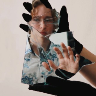 Jugendlicher reflektiert in einem gebrochener Spiegel, dieser wird von Händen in schwarzen Handschuhe gehalten wird.