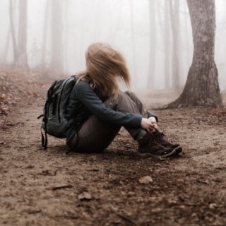 Frau sitzt mit angezogenen Beinen im nebeligen Wald