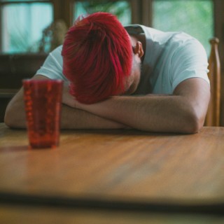 Mensch mit rotem Haar liegt verzweifelt am Tisch
