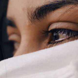 Eine Frau hält Tränen zurück. Ihr Gesicht wird von einem weißen Tuch bedeckt.