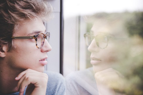 Jugendlicher sieht sein Spiegelbild im Zugfenster