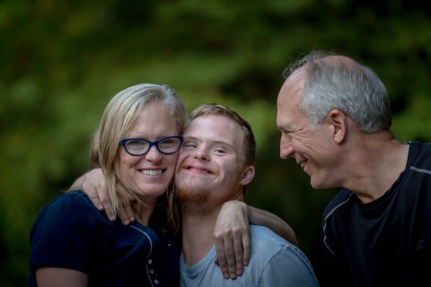 Mutter, Sohn mit Trisomie 21 und Vater umarmen sich